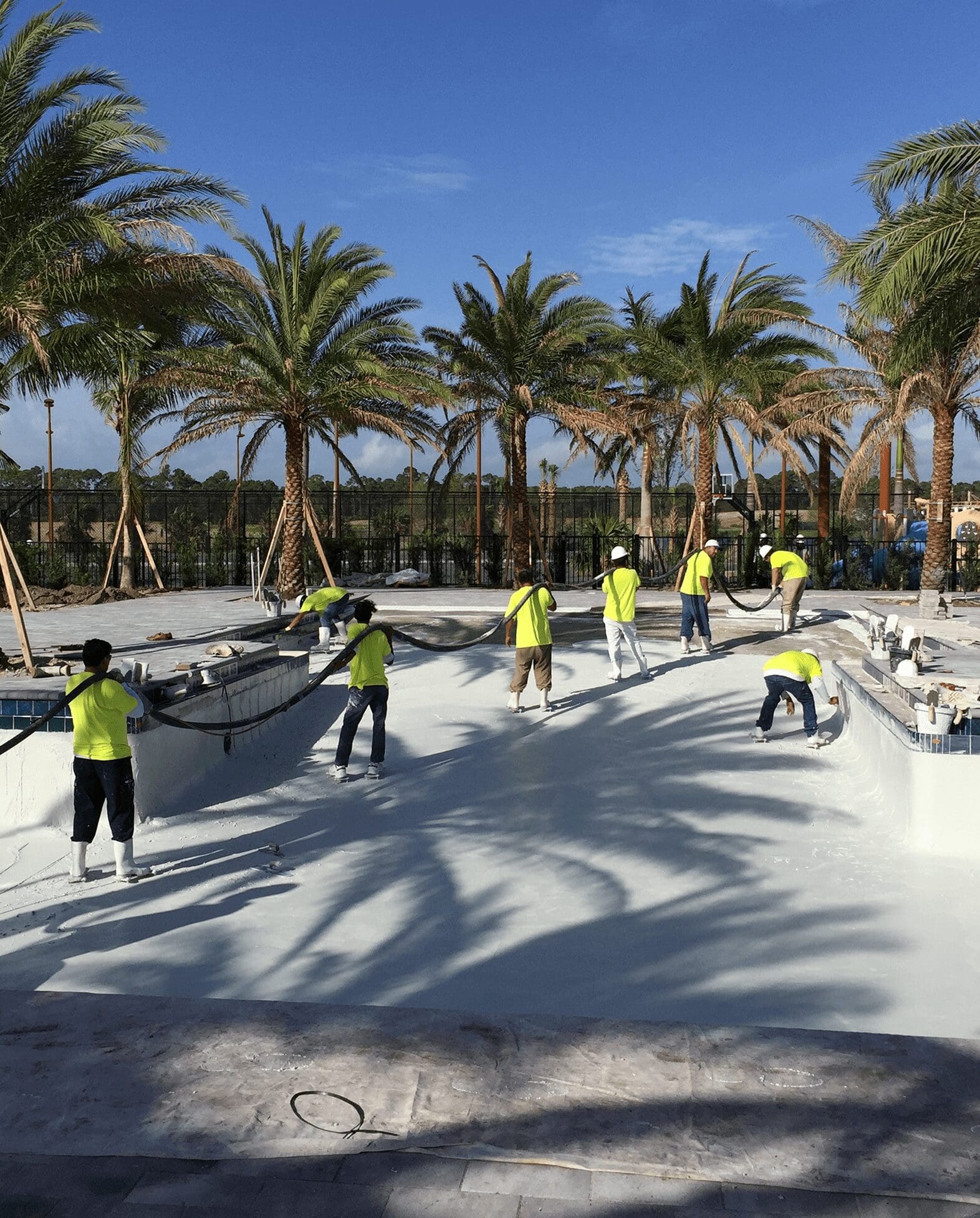 Workers resurfacing empty pool under palm trees